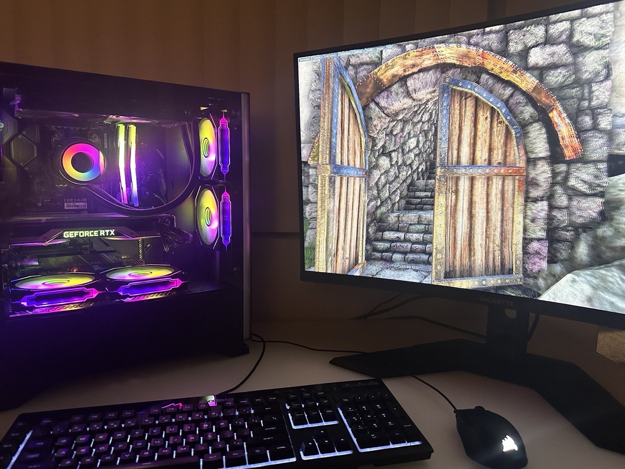 Black PC with multicolored fans beside a monitor showing a stone doorway