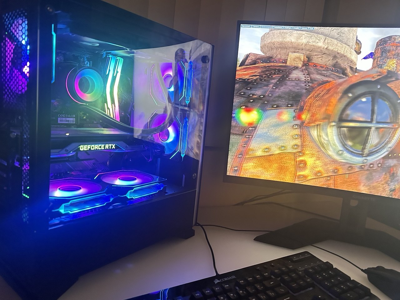 Black PC with multicolored lighting beside a monitor displaying a game