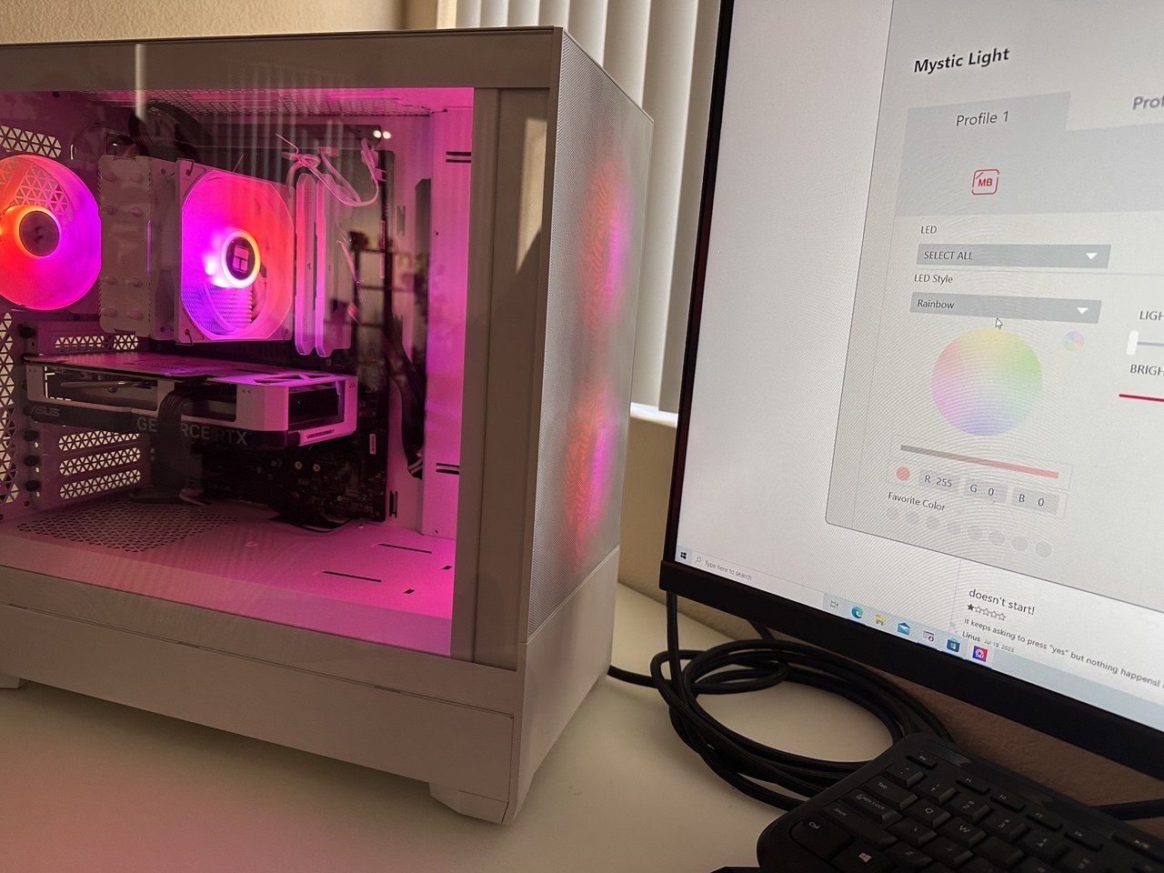 White PC case with pink-lit fans and a tower-style processor cooler beside a monitor