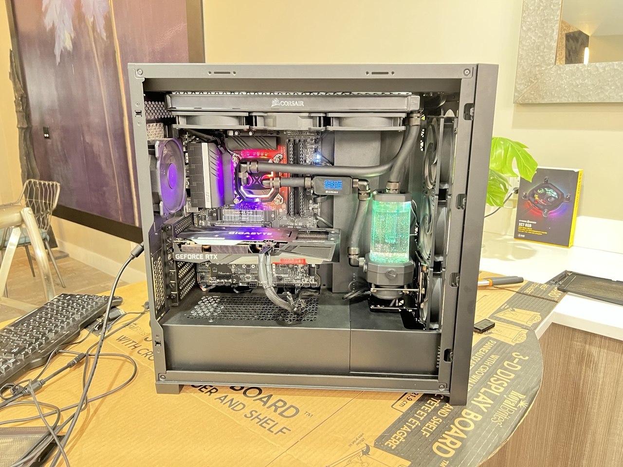Open black PC case with cooling tubes, reservoir and purple-lit components on a work surface