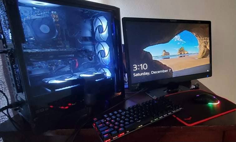 Blue-lit black PC beside a monitor, keyboard and illuminated mouse